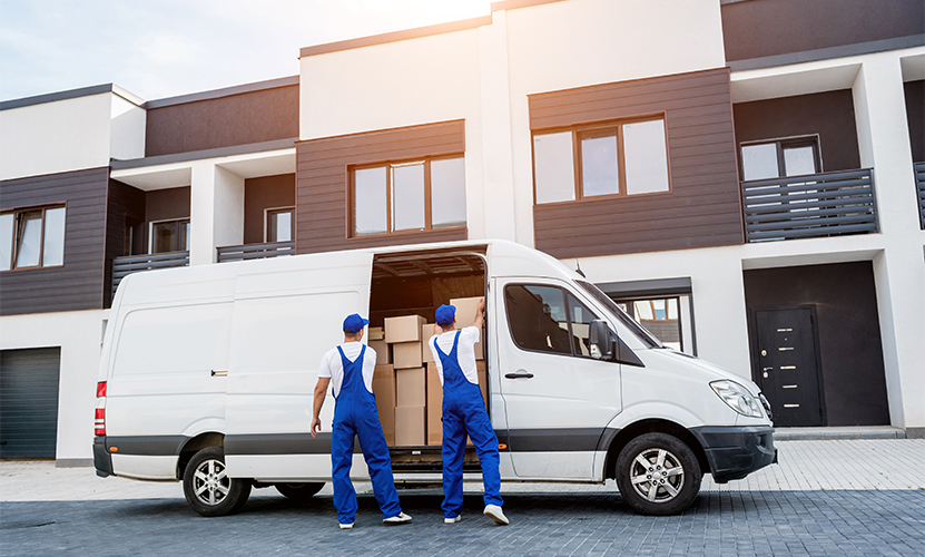Two removal company workers unloading boxes from minibus into new home